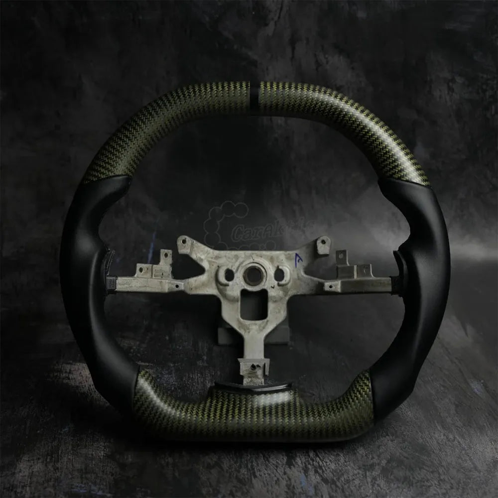 Custom gold carbon fiber steering wheel for 2006-2013 Chevrolet Corvette C6, featuring premium black smooth leather grips, a black center stripe, and flat bottom design on a dark industrial background.