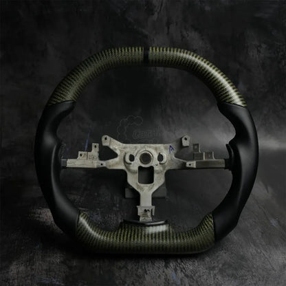 Custom gold carbon fiber steering wheel for 2006-2013 Chevrolet Corvette C6, featuring premium black smooth leather grips, a black center stripe, and flat bottom design on a dark industrial background.