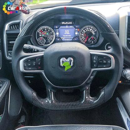 Installed custom carbon fiber steering wheel on a 2019-2025 Ram 1500 interior, featuring glossy carbon fiber trim, red top racing stripe, and smooth black leather grips.