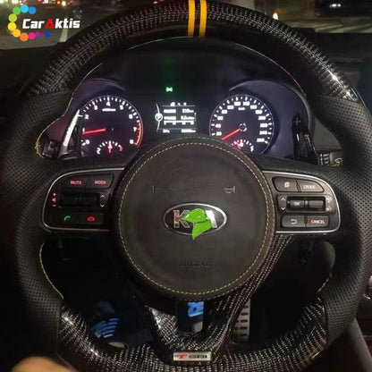 Interior view of a 2016-2020 Kia Optima featuring an installed custom steering wheel with glossy black carbon fiber and premium black perforated leather for a sleek, OEM+ look.
