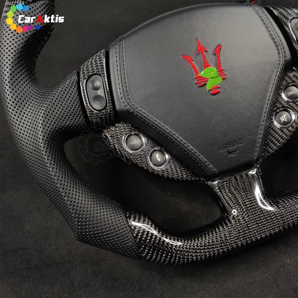 Detail view of carbon fiber control bezels and Maserati trident logo on a custom steering wheel.