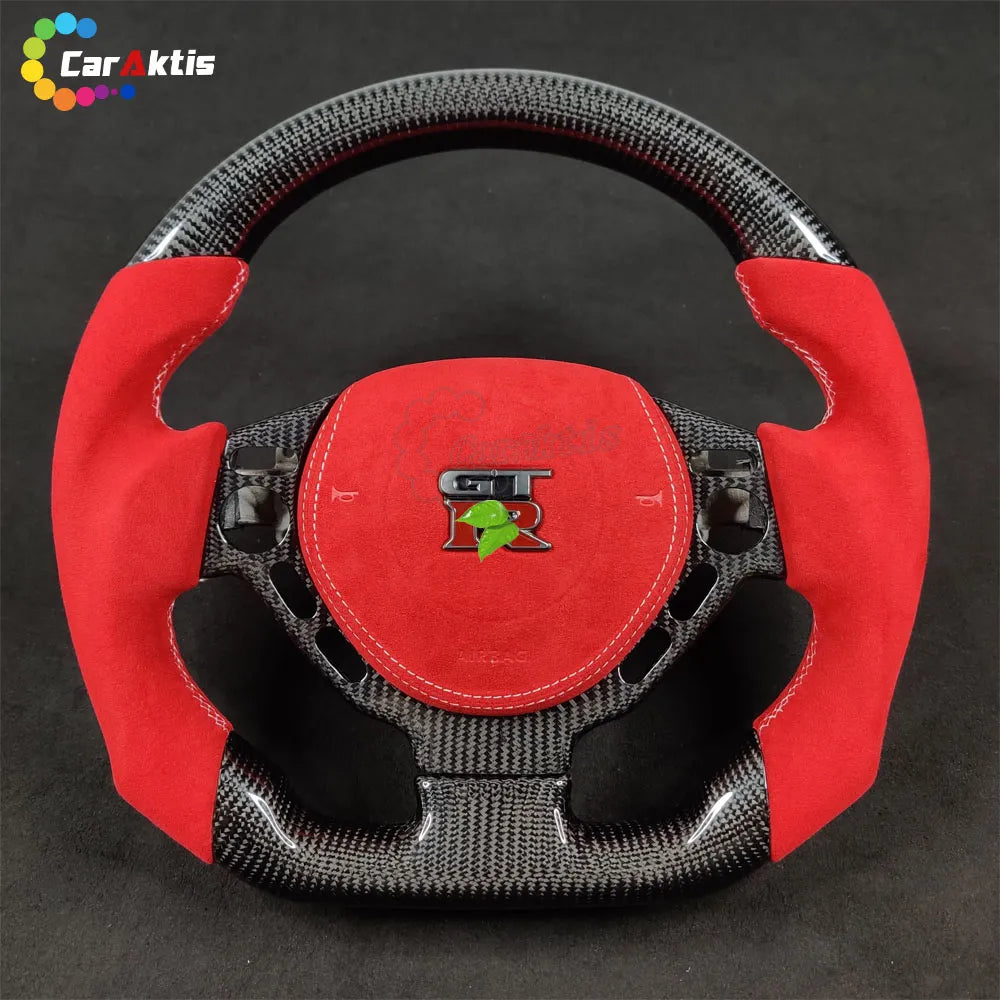 Nissan GT-R R35 custom steering wheel with gloss carbon fiber finish, red suede grips, and GT-R logo airbag cover.