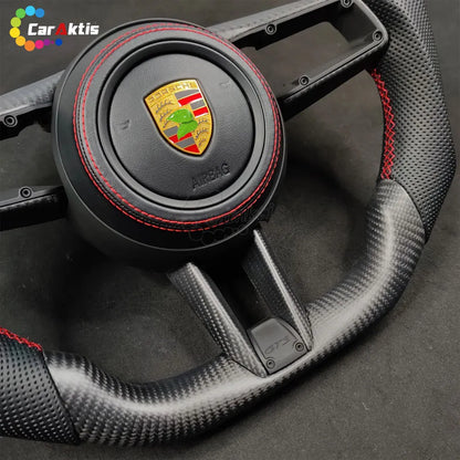 Angled view of a Porsche 992 custom steering wheel with premium red stitching and ergonomic carbon fiber thumb rests.