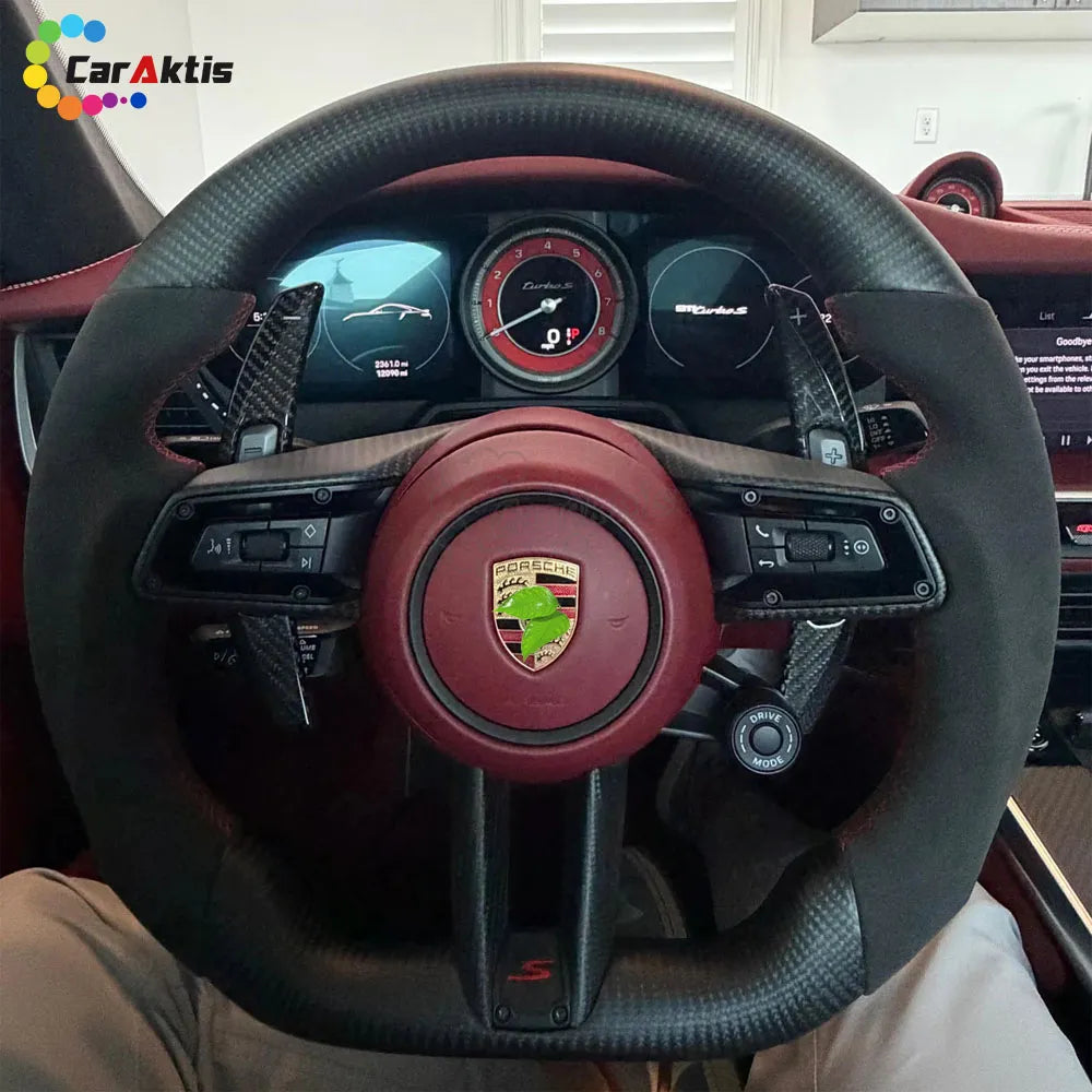 Interior view of a Porsche 911 992 Turbo S featuring a custom carbon fiber and Alcantara steering wheel with red accents.