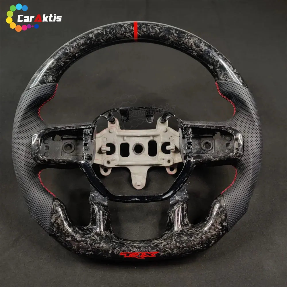 Forged carbon fiber steering wheel with black perforated leather grips and red TRX branding on the bottom flat base.