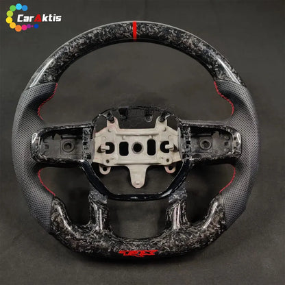 Forged carbon fiber steering wheel with black perforated leather grips and red TRX branding on the bottom flat base.
